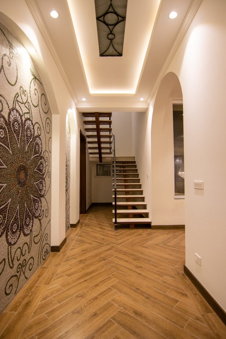 Modern living room interior with warm peach and white marble walls, an orange armchair, indoor green plants, and large windows allowing 
                       natural sunlight to fill the space.