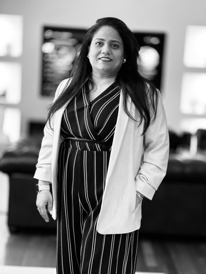 Professional woman standing confidently indoors, wearing a striped outfit and light blazer, smiling in a modern office setting.
