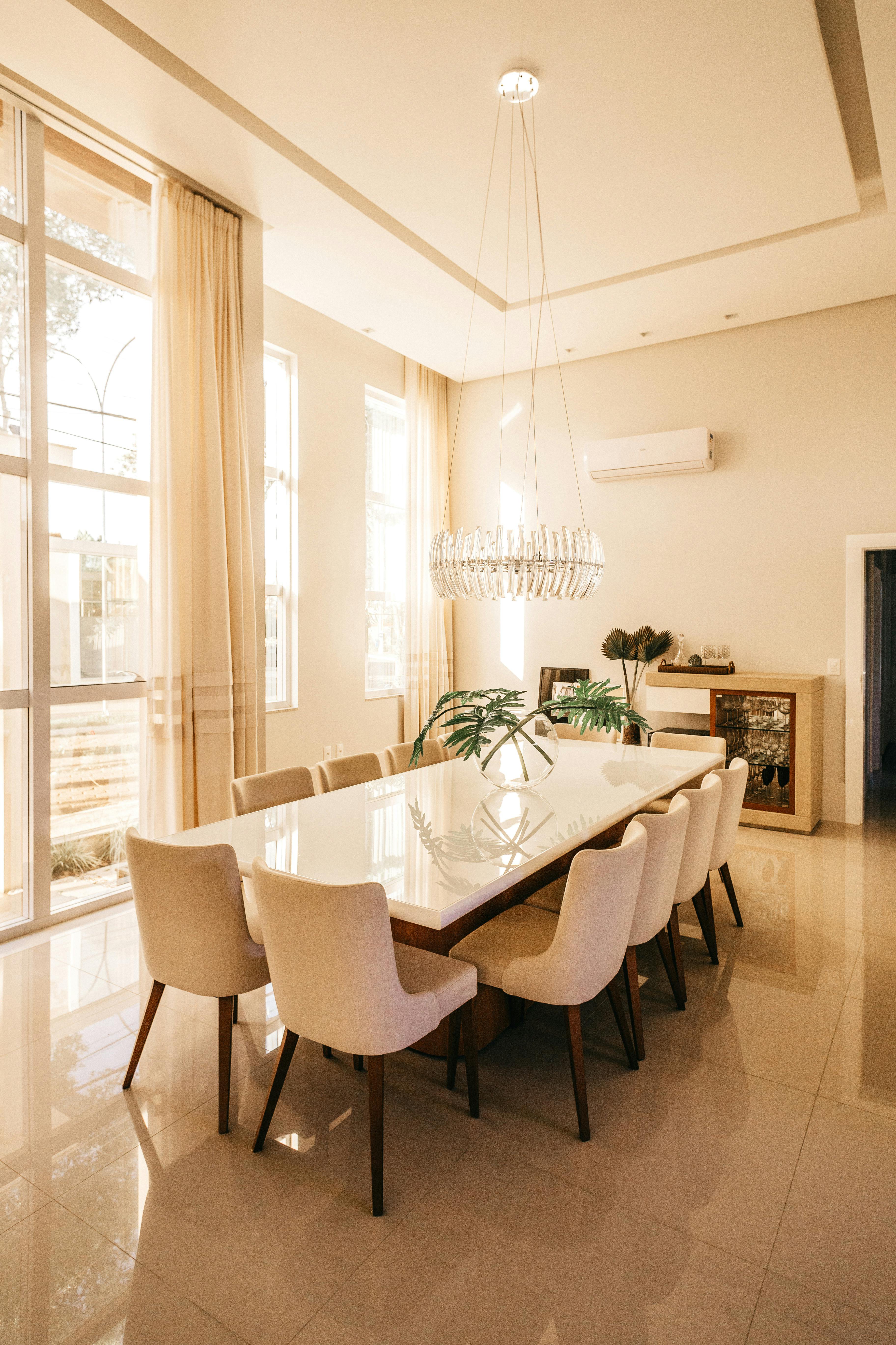 Elegant dining room with a long table, eight white chairs, and modern chandelier. 